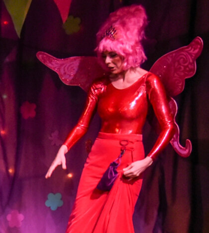 The Fairy Godmother in a floor-length red gown with red wings and a shock of pink hair.