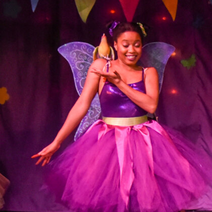Pippa in a purple dress with patterned wings, mid-dance on the stage.