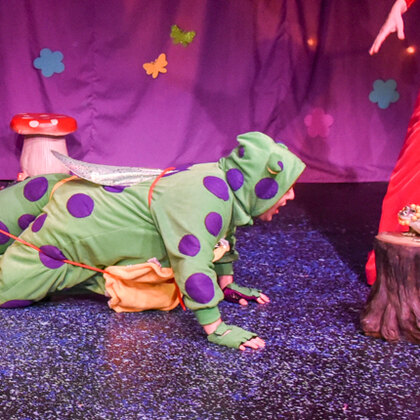 Scruffy, a green dragon with purple spots and silver wings, sprawled flat across the stage.