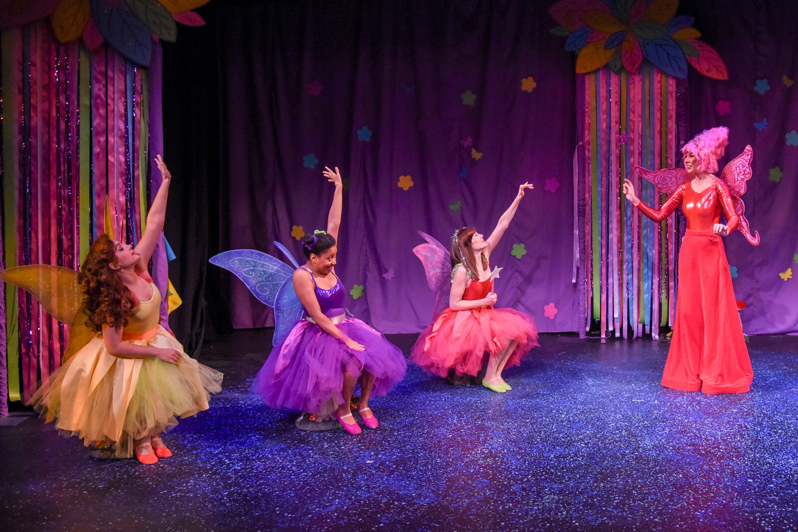 Four fairies in gold, purple, coral and red costumes reaching upward together in the Sparkle Tree Forest.